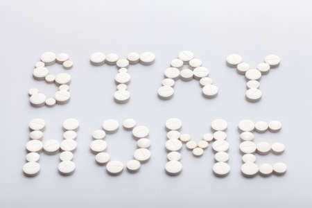 Stay home inscription made of round white pills on a white background, medical concept on the theme of the coronavirus strain covid-19 quarantine with copy spce.の写真素材