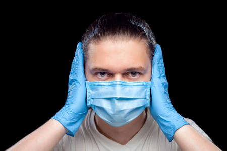 Deaf male portrait of a doctor in a medical mask and surgical gloves covers his ears with his hands so as not to hear anger isolated on a black background concept .の写真素材