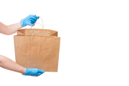 hands in sterile gloves of a courier for the safe delivery of goods in an eco friendly package shows...