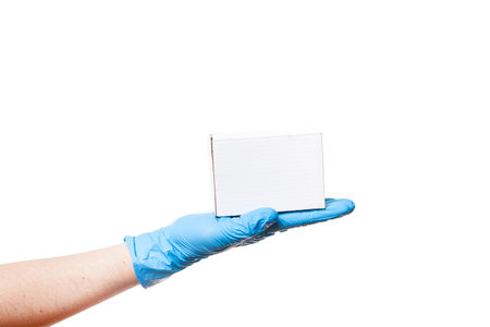 Delivery man's hand in a blue sterile latex glove holds a white unlabel cardboard box on palm, safe...