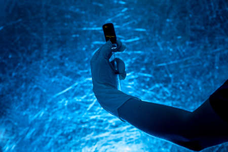 syringe with glass bottle for vaccination in hand in medical glove silhouette on a blue background, close up background on a medical theme in dark colors.の写真素材