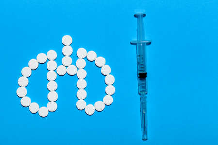 lungs symbol made of white round pills and a syringe with a vaccine on a blue background with copy space.の写真素材