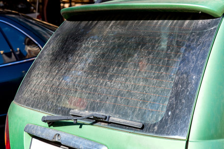 dirty green car in a layer dry dust, rear view on an unwashed rear window with a faulty wiper on sunny day, close-up background on a car theme.の写真素材