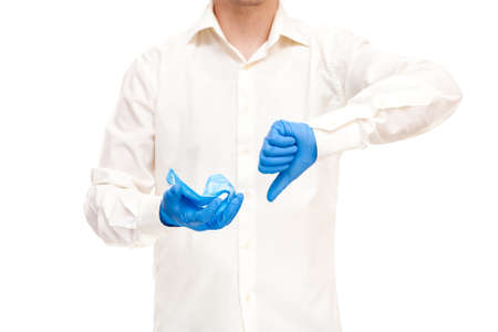 protest against the use of ineffective means of protecting medical masks, concept on medical theme doctor with gloves holds mask and shows thumb down gesture faceless isolated on white.の写真素材