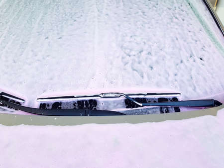 Close-up of the front windshield with a wiper covered with a washing active foam for washing a car.の写真素材