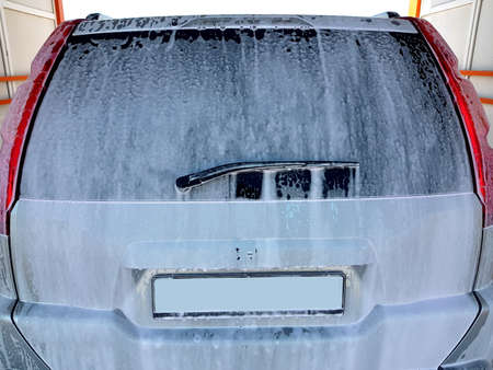 rear trunk lid with window wiper blade coated with detergent active foam with bubbles for washing car, closeup back view on suv car nobody with copy space at the self-service car wash.の写真素材