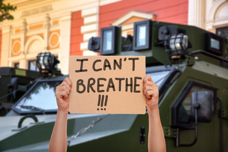 cardboard protest poster hold hand with message i can't breath on background armored military...