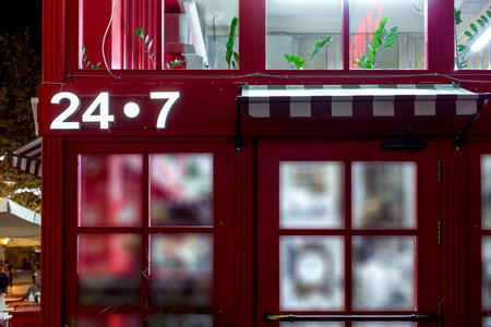 entrance to the red store with a canopy above the door with a luminous signboard 24/7 round the...