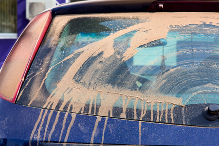 dirty car hatchback covered with a dry layer of dust from clay smeared with a windshield wiper...