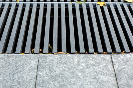 grating of the drainage storm system on the pedestrian park sidewalk made of gray stone granite...