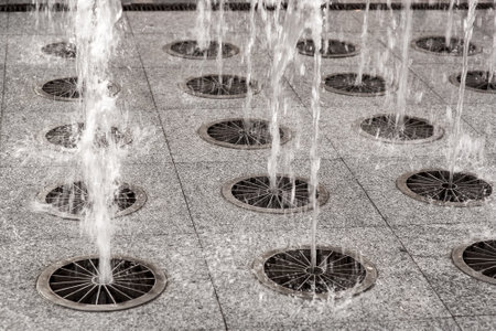 ground fountain from a stone sidewalk, jets of water under pressure beat upwards, splashing water along the pedestrian sidewalk of city scape close up details, nobody.の写真素材