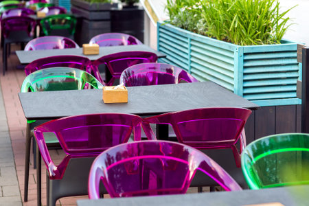 a wooden table top with a napkin holder and plastic multi-colored chairs on the terrace of a street cafe with free seats, nobody.の写真素材