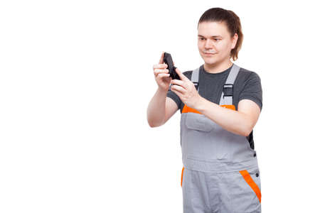 brunette with long hair male employee in gray uniform of car mechanic worker with spanner wrench in his pocket holds brake pads in his hands isolated on white background man with car spare parts.の写真素材