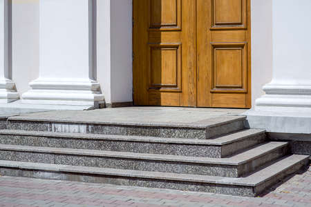granite steps of a staircase with a threshold at the entrance to the wooden door of the temple with white walls illuminated by sunlight architectural building, nobody.の写真素材