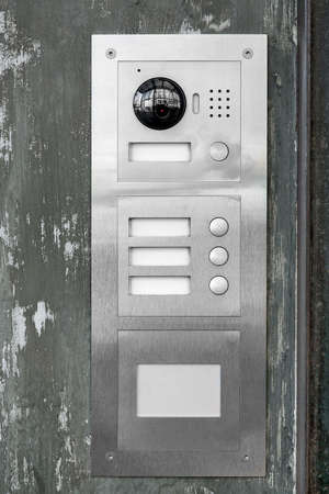 gray iron intercom with call buttons and a camera with a speaker outdoor security system on the facade of the building at the entrance close-up, nobody.の写真素材