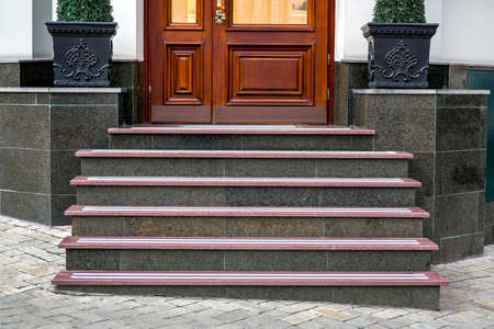 a marble staircase with granite steps to a wooden entrance door with a threshold and pedestals for flowerpots with bushes at the front of the building front view, nobody.の写真素材