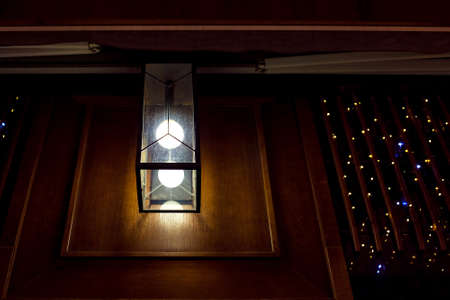 square glass lantern with light bulb on wooden wall of retro architecture building facade, night city scene close-up.の写真素材