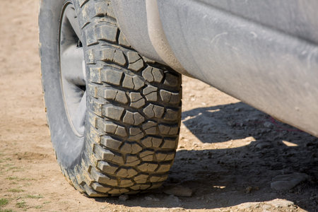 muddy off-road tire with rough tread for 4x4 four-wheel drive cars on rural clay pavement close-up.