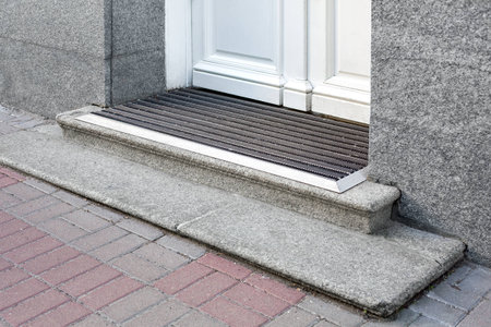 stone threshold with foot mat at the entrance door made of white wood and gray stone facade cladding...