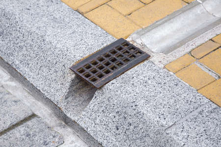 Drainage system grate, grill for removal of rainwater from walking paths through ditch and hole in granite curbe on the road engineering structures close up, nobody.の写真素材