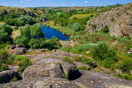 natural landscape of the canyon with granite rocks on the top of the cliff on a sunny summer day, a mountain river with a lake and reeds in the valley at the foot of the valley below, nobody.の写真素材