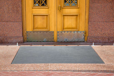 stone threshold with foot mat at the entrance door made of wood and granite stone facade cladding of retro European architecture building closeup front view on sunny day, nobody.の写真素材
