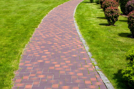 curved stone tile pavement crescent, path in park landscaped with green grass and bushes, garden...