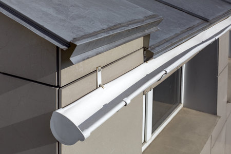 roof gutter made of stainless sheets of white color rainwater drainage pipe close-up on the corner...