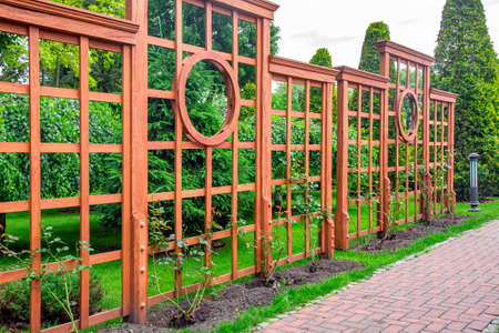 Vertical pergola made of wood in a rose garden with a stone tile walkway and ground lantern in the backyard in a garden with plants and a green lawn on a spring day, nobody.の写真素材