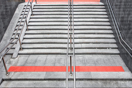gray border staircase with steps and stainless steel handrail descent into the underpass, entrance to subway with tactile red tiles and ramp urban improvement for disabled, top view, nobody.の写真素材
