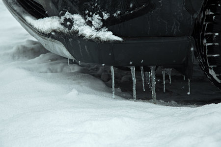 black parked car covered with icicles on the bumper on a winter cold day, close-up of a vehicle and ice with snow, nobody.の写真素材