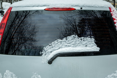 rear window of car with windshield wiper covered with snow and blocked, gray vehicle with red brake lights, nobody.の写真素材