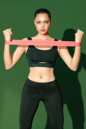 Beautiful strong happy cheerful young Asian sports woman does stretching isolated on green...