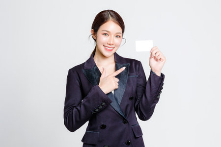 Attractive cheerful young Asian businesswoman wearing formal suit and smiling while standing and holding credit card on isolated white background in studio.の写真素材