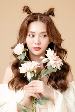 Young Asian beauty woman curly long hair with korean makeup style on cute face and perfect skin holding flowers on isolated beige background. Facial treatment, Cosmetology, plastic surgery.の写真素材