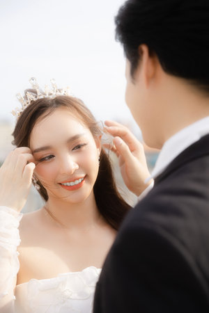 Lovely Asian bride looking at her groom feel in love on the rooftop in a romantic outdoor hotel. Beautiful couple in wedding attire.の写真素材