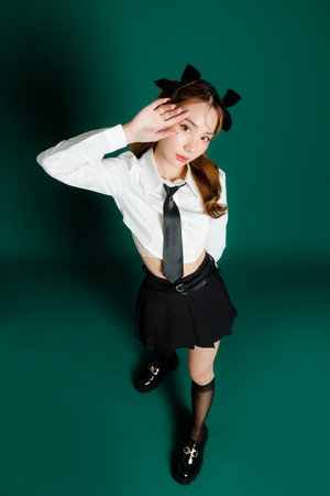Portrait of pretty joyful teenage Asian student woman in white shirt and black short skirt with slim body posing on isolated green background People lifestyle concept. Mock up copy space.の写真素材