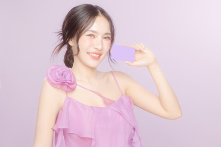 Young Asian beauty woman model pull back hair with natural makeup look on face and perfect clean skin hold card on violet background. Facial treatment, Cosmetology, Spa, Aesthetic, plastic surgery.の写真素材