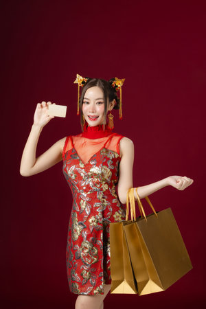 Beautiful Asian woman with clean fresh skin wearing traditional cheongsam dress holding credit card Gold shopping bags on red background. Happy Chinese new year.の写真素材