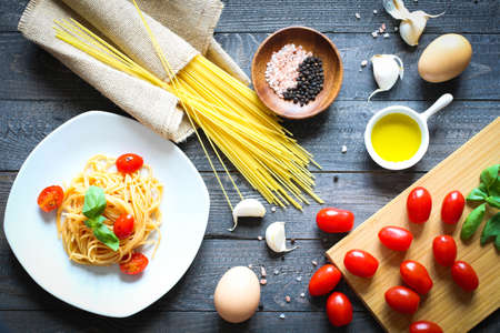 Top view of italian ingredients for tomato and basilic spaghetti with olive oil and garlic over a wood background.の写真素材