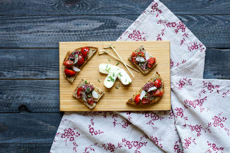Italian bruschetta made with toasted slices of bread with olives, cherry tomatoes and  olive on a  Board over dark wooden backgroundの写真素材