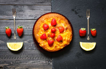Lemon cake with strawberries, sugar end chocolate over an old wooden table with decorative napkins.の写真素材