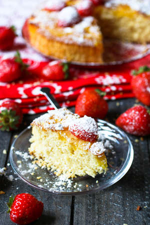 Lemon cake with strawberries, sugar end chocolate over an old wooden table with decorative napkins.の写真素材