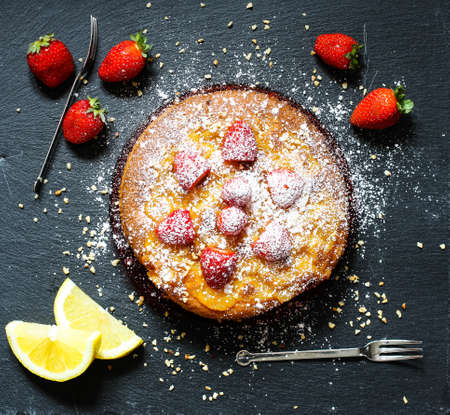 Lemon cake with strawberries, sugar end chocolate over an old wooden table with decorative napkins.の写真素材