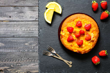 Lemon cake with strawberries, sugar end chocolate over an old wooden table with decorative napkins.の写真素材