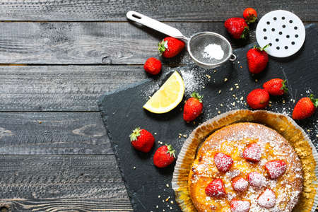 Lemon cake with strawberries, sugar end chocolate over an old wooden table with decorative napkins.の写真素材