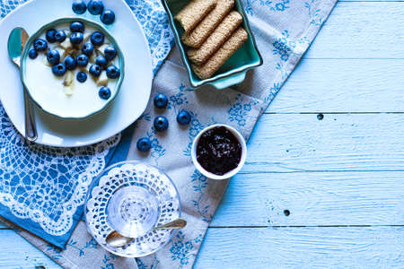 Healthy Breakfast with blueberries and banana yogurt, biscuits, marmalade, coffee and peaches over a light wooden background.の写真素材