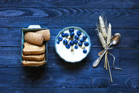Healthy Breakfast with blueberries and banana yogurt, biscuits, marmalade, coffee and peaches over a light wooden background.の写真素材