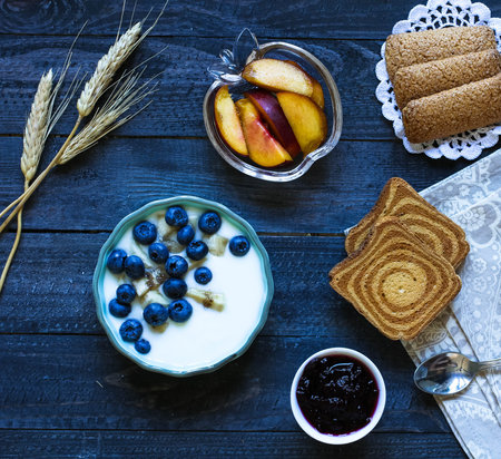 Healthy Breakfast with blueberries and banana yogurt, biscuits, marmalade, coffee and peaches over a light wooden background.の写真素材