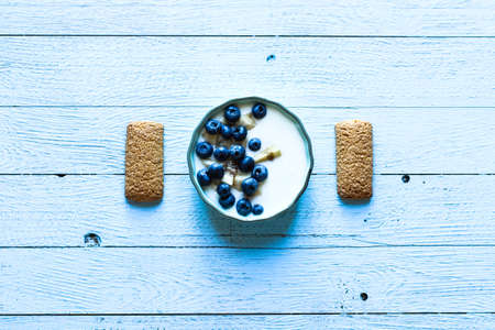 Healthy Breakfast with blueberries and banana yogurt, biscuits, marmalade, coffee and peaches over a light wooden background.の写真素材